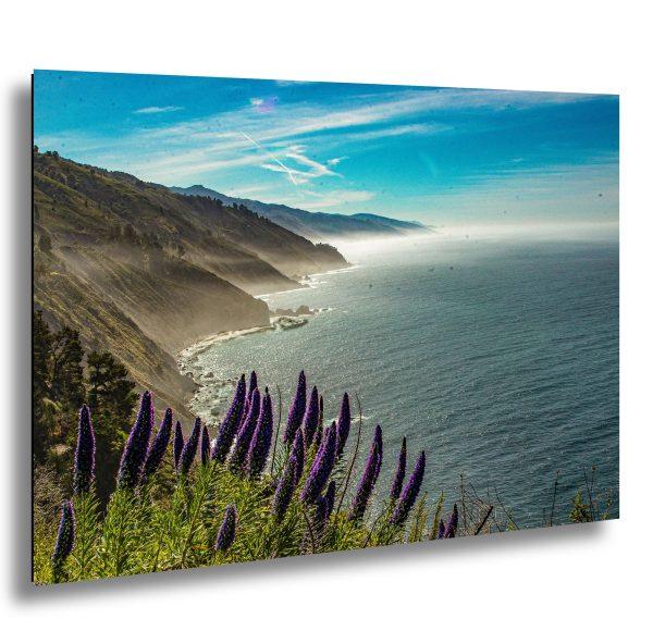 Big Sur coastline with purple wildflowers, misty cliffs, and turquoise Pacific Ocean.